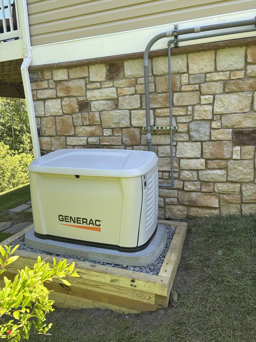Generac standby generator on a new pad beside a stone wall